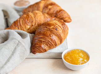 Croissants on wooden cutting board with jam and chocolate cream, light concrete background.