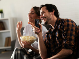 Young loving couple relaxing and laughing on sofa together. Happy couple watching movie at home..