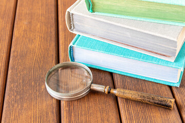 An old magnifying glass and a stack of books on a wooden table. The concept of getting knowledge...
