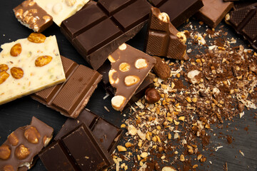 a lot of different types of chocolate and various ingredients such as nuts and cocoa powder lie on a black wooden plate photo taken from above