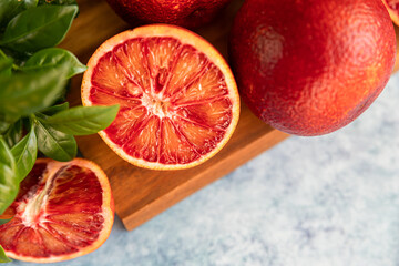 Sliced and whole ripe juicy Sicilian blood oranges on wooden cutting board with mint, blue concrete...