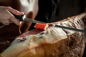 butcher cuts jamon with knife. Iberian ham cutter. Dry Spanish ham, Jamon Serrano, Bellota, Italian Prosciutto Crudo or Parma ham