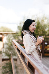 girl leaned on the railing and holds a tin mug in her hands