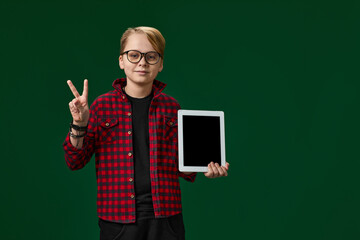 caucasian child boy in red checkered shirt shows empty tablet on green background