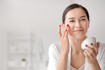 Beautiful young woman applying facial cream in bathroom, closeup