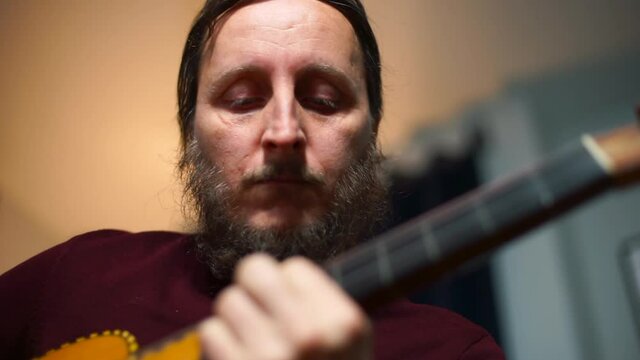 The musician plays the guitar. He quickly moves his fingers along the strings, makes a melody. Moves his head to the beat of the music. Creative inspiration.