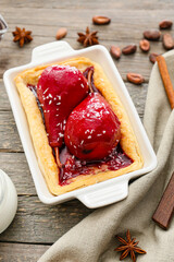 Baking dish of tasty poached pears in wine sauce on wooden background