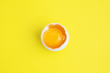 Raw chicken egg white and yolk in half shell on yellow background. Top view.