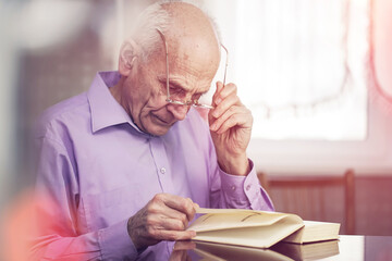 Bright sun light illuminated senior man reading book at table.