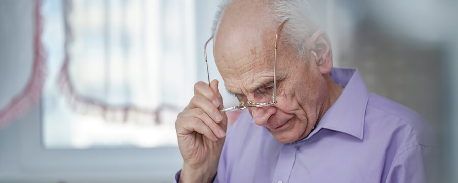 Old grey haired man wearing eyeglasses writes or reads over table