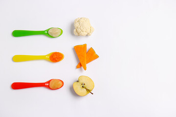 Spoons with different baby food and ingredients on white background