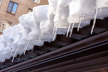 the edge of a roof covered by snow, ice and icicles against the wall of another house