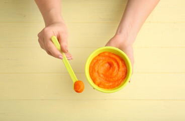 Woman holding bowl and spoon with tasty pumpkin puree on color background