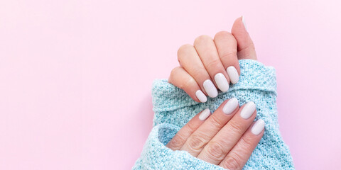 Female hands in blue knitted sweater with beautiful manicure - white ivory nails on pink paper...