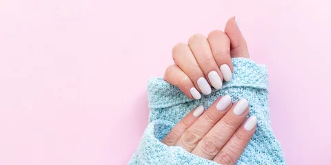  Female hands in blue knitted sweater with beautiful manicure - white ivory nails on pink paper background, template banner with copy space © MariiaDemchenko