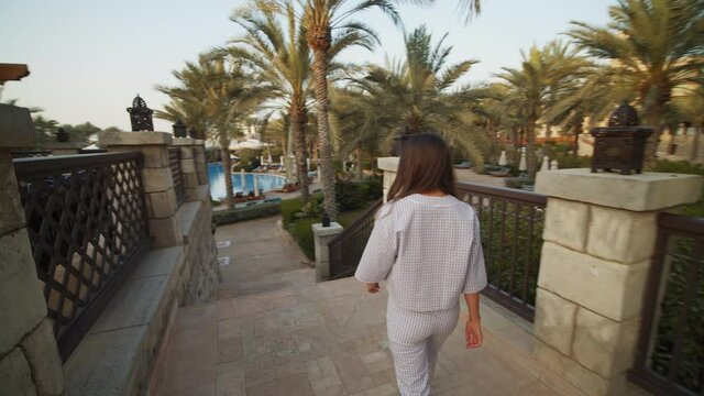 Woman walking down the stairs in luxury tropical resort with pool in Dubai. Back view of attractive brunette walking in Dubai tourist resort