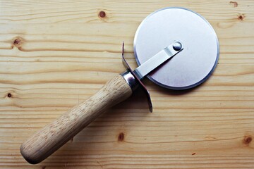 Pizza slicer on the bright wooden board.