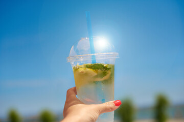 cool refreshing lemonade in hand. woman holding ice invigoration summer drink in transparent plastic glass