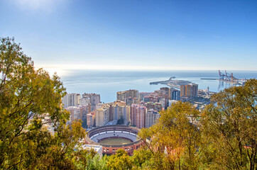 Bull arena in the middle of Malaga cityscape, port and blue sky in the background. Malaga, Andalusia, Spain.