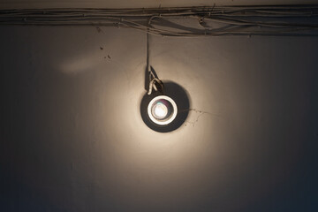 An incandescent light bulb with cobwebs and dirt illuminates the white wall in the entrance of the house