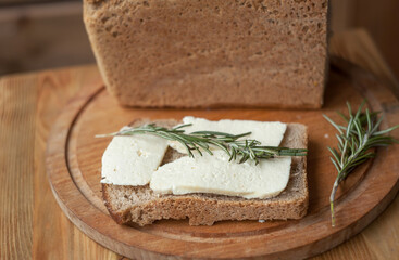 .sandwich with homemade young white cheese and black rye bread on a wooden board