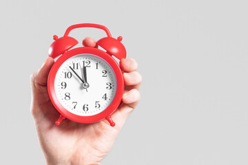 Analog red alarm clock in hand on a white background.