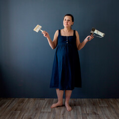 Pregnant woman in a blue dress against a white wall makes repairs, dreams, selective focus