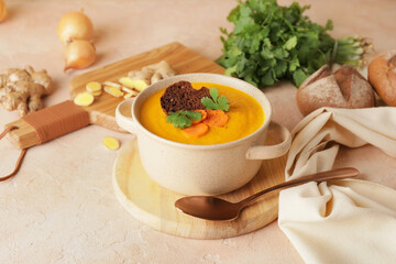 Cooking pot of fresh carrot cream soup on color background