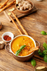 Cooking pot of fresh carrot cream soup on wooden background