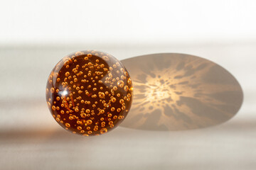 orange glass ball with air bubbles inside illuminated by sunlight on a white-gray background