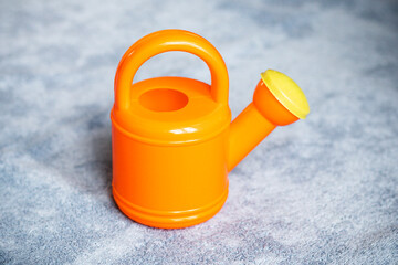 Pomarańczowa zabawka konewka do podlewania ogródka. - obrazy, fototapety, plakaty