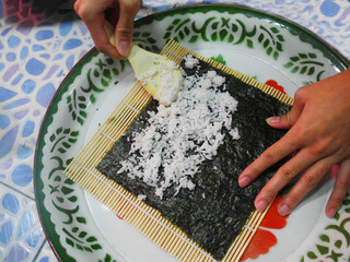 The woman's hand mixes rice and seaweed together to make shushi.