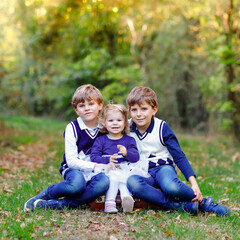 Fototapeta premium Portrait of three siblings children. Two kids brothers boys and little cute toddler sister girl having fun together in autumn forest. Happy healthy family playing, walking, active leisure on nature