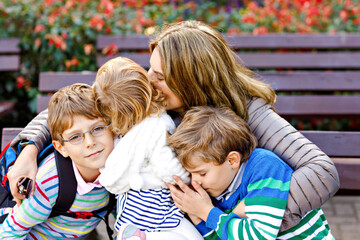 Fototapeta premium Mother and three children hugging. Happy family sitting outdoor: woman and two brother kids boys and cute little toddler girl. Siblings and mum in love. Healthy people giving hugs.