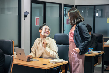 Asian businesswoman consulting with happy and smiling colleague wearing face shield at desk in modern office