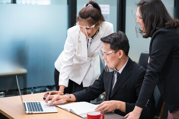 Asian female manager consulting and collaborating with colleagues working with laptop at desk in the office