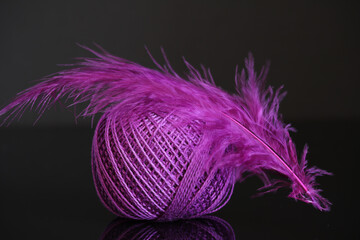 Lilac spool of thread for knitting with a lilac feather on a black background.