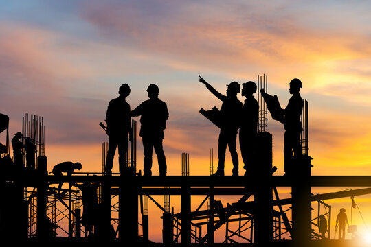 Silhouette Of Engineer And Worker On Building Site, Construction Site At Sunset In Evening Time.