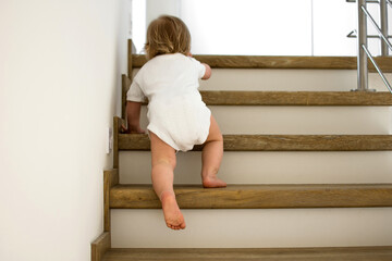 Little caucasian baby is crawling on stairs at home in sunny interior. Lifestile photography. Child...