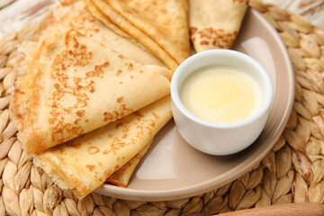 Plate with thin pancakes and condensed milk on table