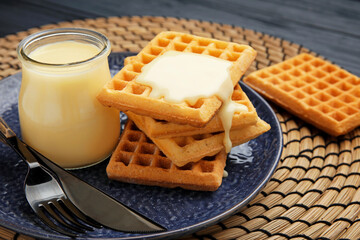 Jar with sweet condensed milk and waffles on table