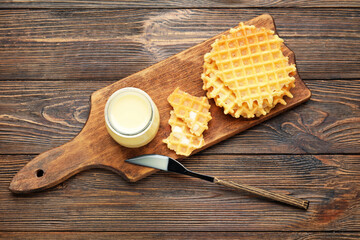 Fototapeta na wymiar Jar with sweet condensed milk and waffles on wooden background