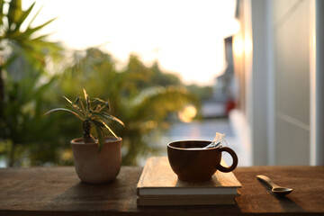 Wooden cup and notebook with plant pot on wooden table under sunset light