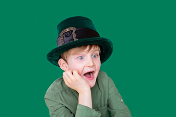 A closeup portrait of very surprised, shocked preteen boy in carnival St. Patrick's Day hat on green backgroundwhite. Copy space.