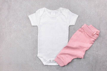 White baby girl bodysuit mockup on the gray concrete background with pink panties. Design onesie template, print presentation mock up. Top view. Flat Lay.