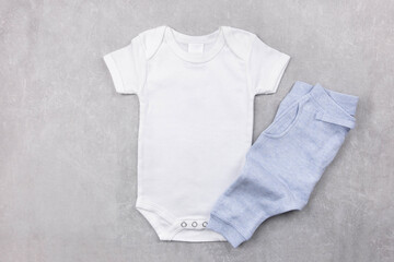 White baby girl or boy bodysuit mockup on the gray concrete background with blue panties. Design onesie template, print presentation mock up. Top view. Flat Lay.