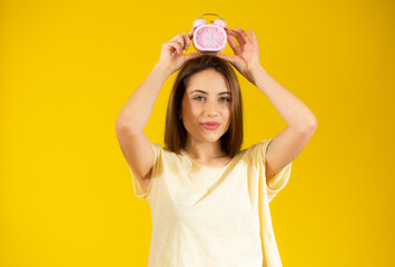 Portrait of cheerful young woman holding alarm clock isolated over yellow background