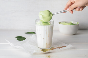 Woman preparing tasty dalgona matcha latte on light wooden background