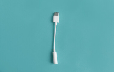An adapter for a USB to 3.5mm type c headphone cable on a smartphone. White cable close-up, 3.5 mm audio cable on a blue background. view from above