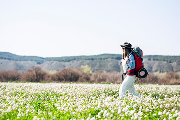 Woman with red backpack and hat walking through flowery field